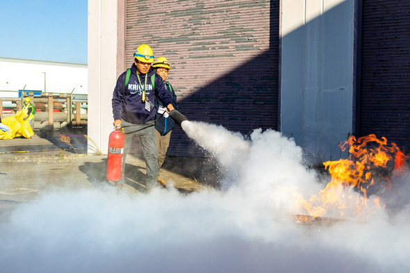 Two people use a fire extinguisher to douse a flame 