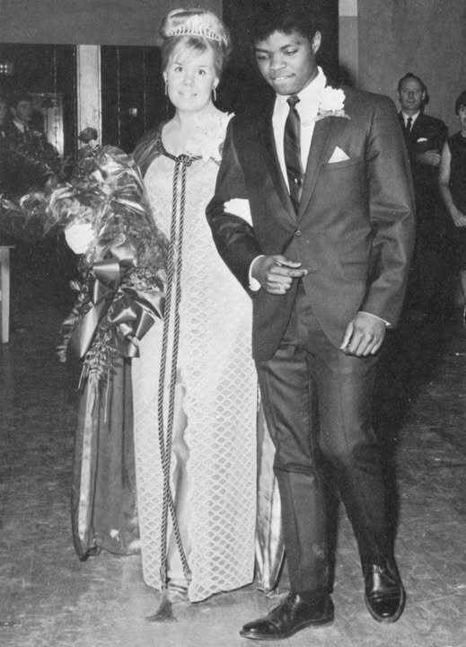A white woman and a black man holding arms at a high school prom in the 1960s
