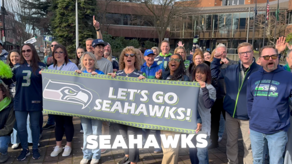 Screen shot of video showing people in Seahawks gear in a plaza with the words Seahawks on the screen 