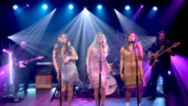 Three women standing on a stage singing 