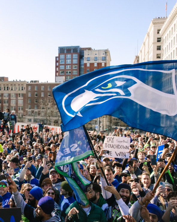 a buncha Seahawks fans at a parade with a big Seahawks flag in the foreground 