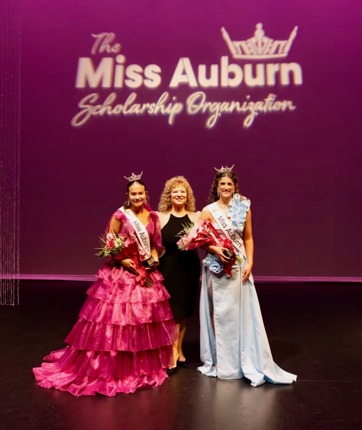 Three people on stage at a pageant with the words Miss Auburn Scholarship above them 