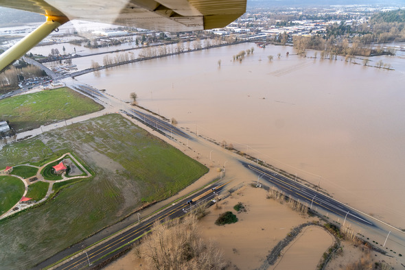 Aerial view of flooded roadway and fields near river during winter storm event.