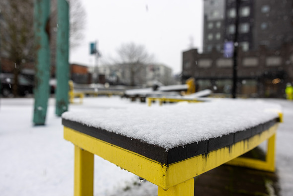 Snow-dusted yellow tables in downtown Auburn with blurred buildings and light snowfall in the background.