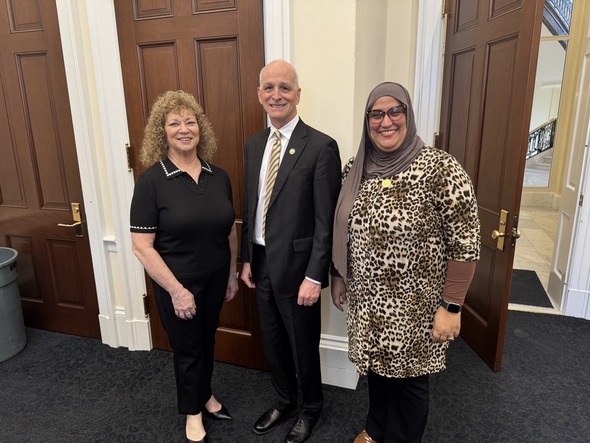 Three people posing together indoors, smiling, dressed in business attire near wooden doors.