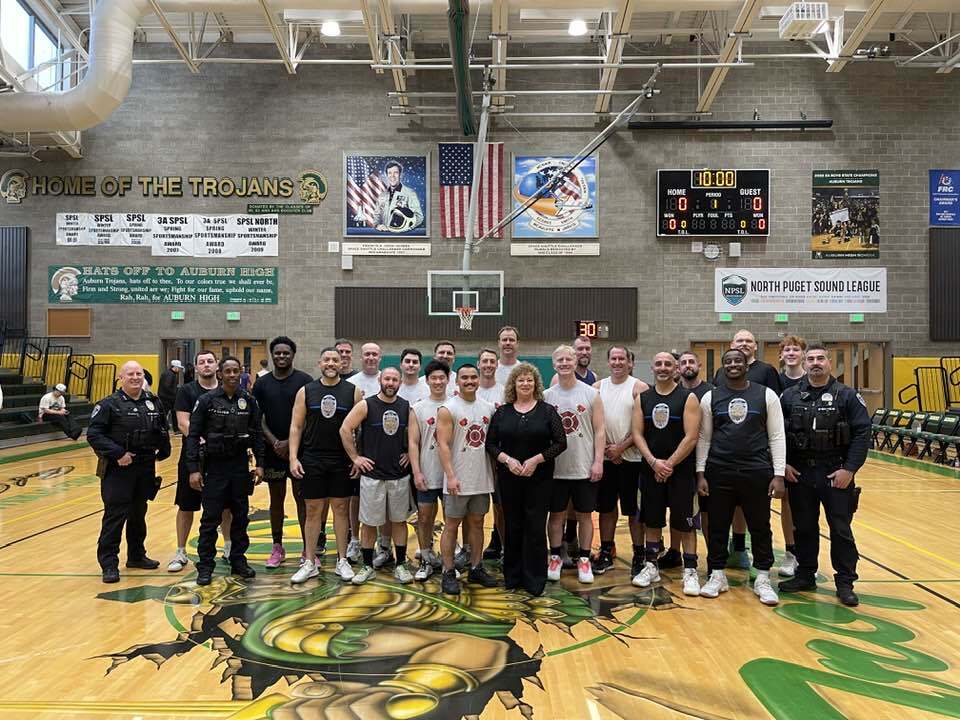Group photo of players, police officers, and community members on Auburn High gym floor after basketball event.