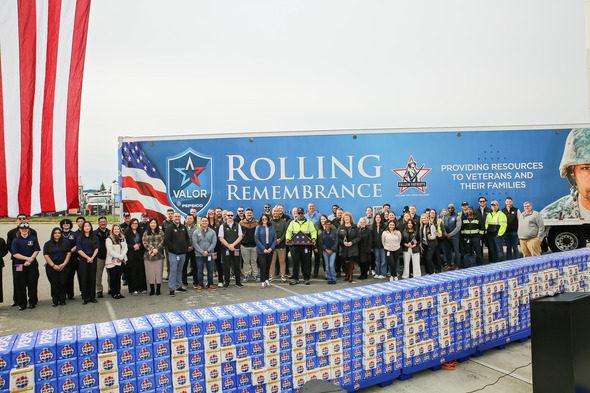 Large group gathered in front of Rolling Remembrance truck and American flag display with stacks of commemorative Pepsi cases.
