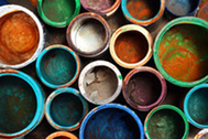 Overhead view of colorful, worn paint buckets with dried residue in shades of blue, green, orange, and white.
