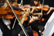 Close-up of violinists playing in an orchestra, bows in motion with sheet music visible.