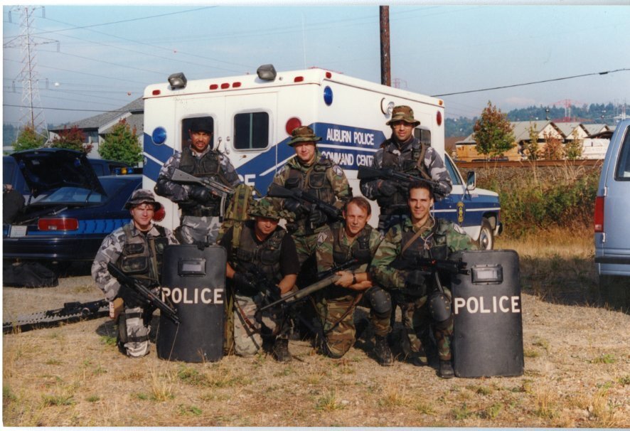 Tactical police team posing with gear and shields in front of Auburn Police command vehicle.