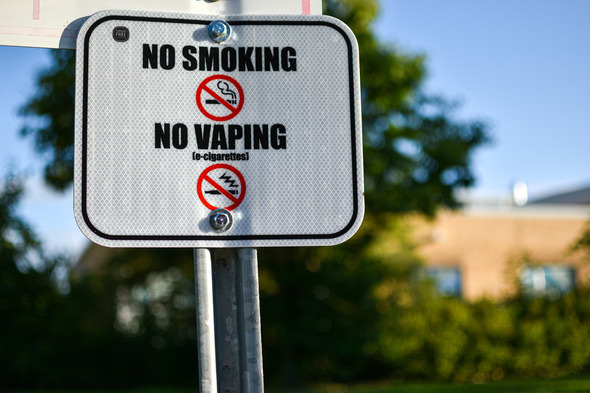 Close-up of a sign reading “No Smoking, No Vaping” with icons on a sunny day.