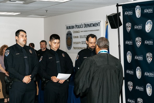 Police officers stand at attention as a judge administers an oath during a ceremony.