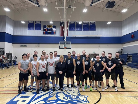 Group photo of firefighters, police officers, and Mayor Backus standing on a gym court.