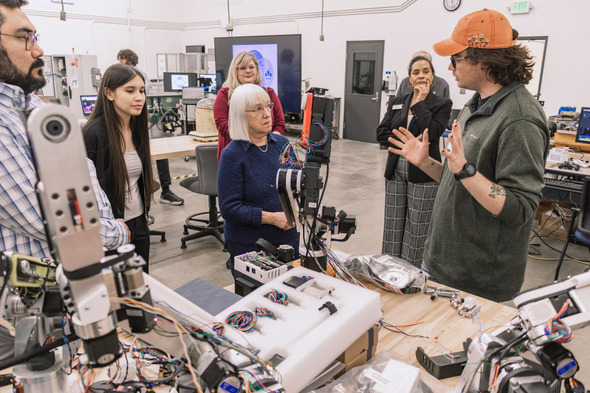 Instructor demonstrates robotics equipment to a small group in a lab, with attendees listening and observing closely.
