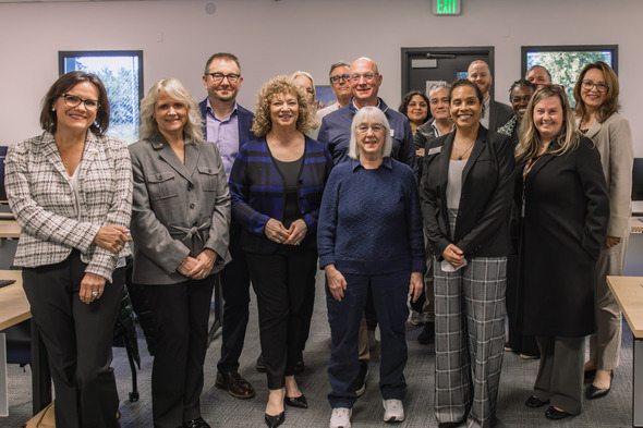 Group of community leaders and partners pose together indoors, smiling during a visit to a technical college.