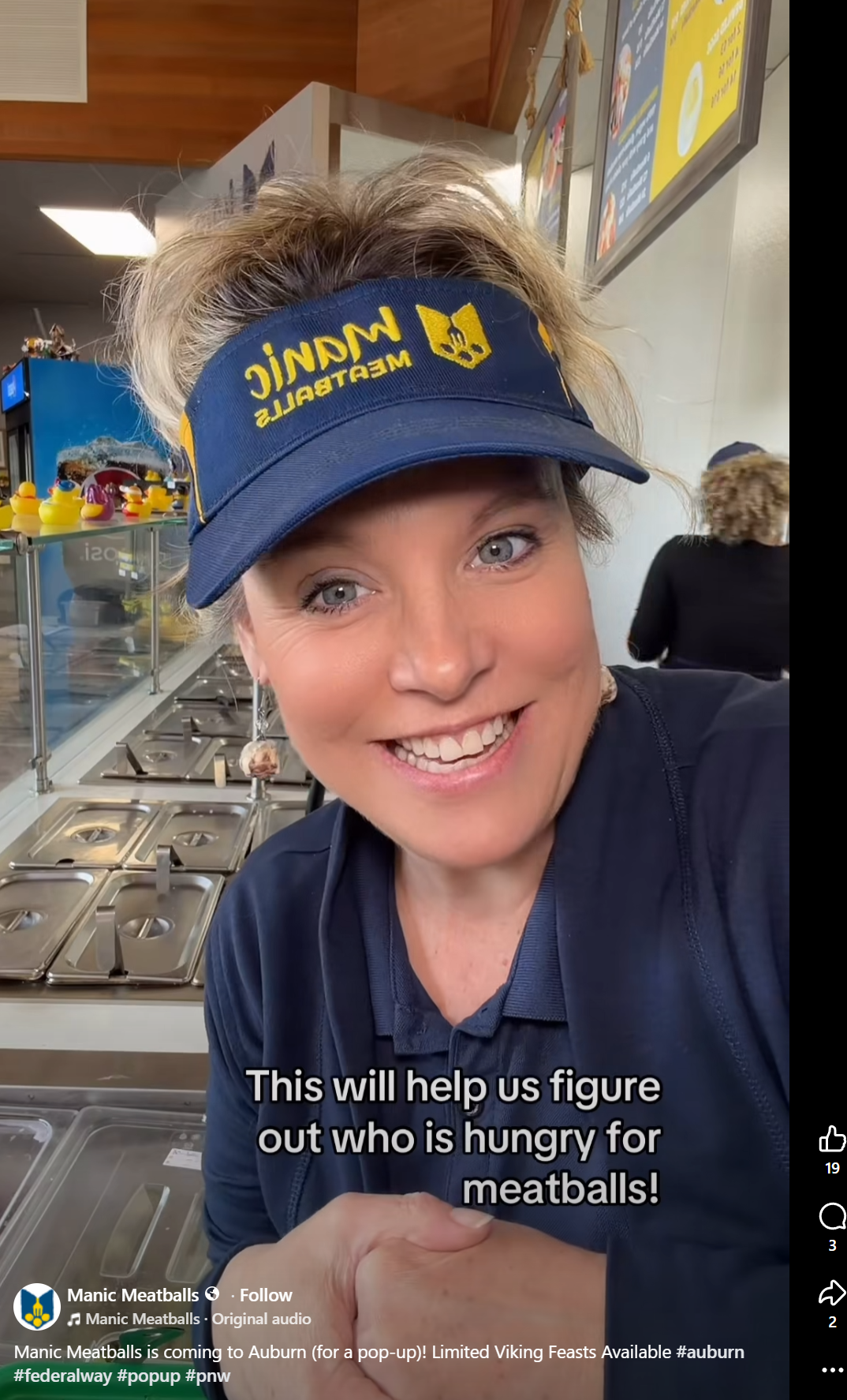 Smiling employee in Manic Meatballs visor behind a food counter, with trays and menu boards visible; caption mentions meatballs pop-up in Auburn.