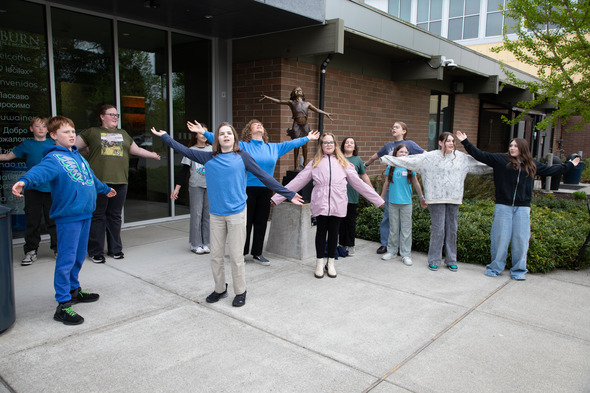 Group of kids posing with arms outstretched outside building near statue, playful and smiling.