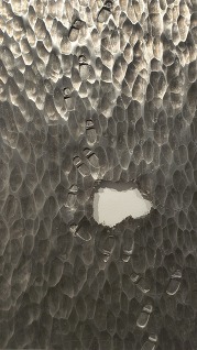 Textured metal artwork with stamped footprints leading to a hole by Reed Peck-Kriss