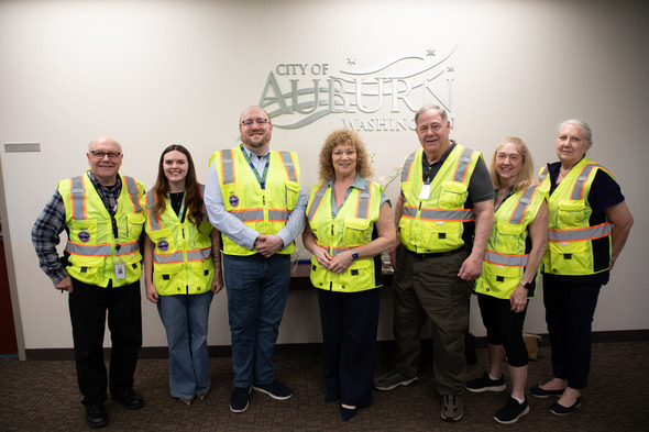 Group of City of Auburn staff in safety vests pose together in front of Auburn city logo.