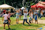 Kids play with bubbles at an outdoor community event with vendor tents and families enjoying a sunny day.