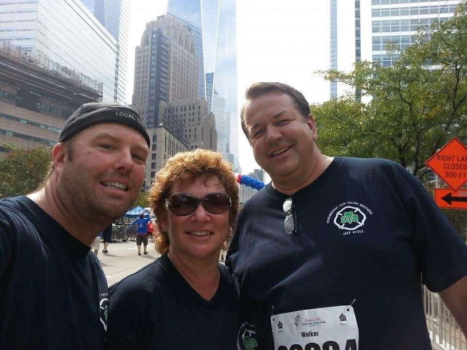 Three smiling adults in race shirts take a selfie on a city street before an event.