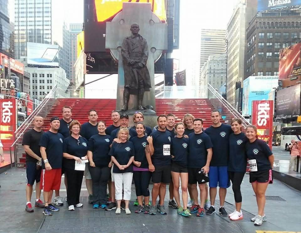 Group in matching shirts posing on red steps in Times Square with statue behind them.