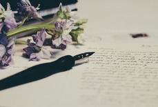 Close up of purple flowers and a single fountain pen resting on page with cursive writing