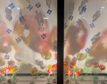 An lit installation of flowers made from single use plastic placed in a gallery space with light reflecting on the walls as large colorful shadows