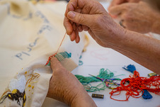 A close up of two hands, with one hand holding a piece of fabric as the other one pulls thread through the fabric with a needle.
