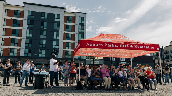 Community members applaud under an Auburn Parks tent during an outdoor ceremony.