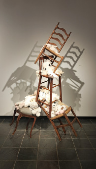 An art piece titled "Balancing Act" by Allison Hyde, depicting a stack of four chairs with stuffed animal toys piled on the seats