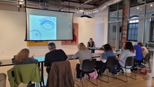 A large group of people sitting at a row of tables drawing and looking up at a screen with sketches of eyes projected