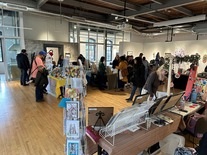 Groups of people browsing at various tables at an indoor art market within a large gallery space