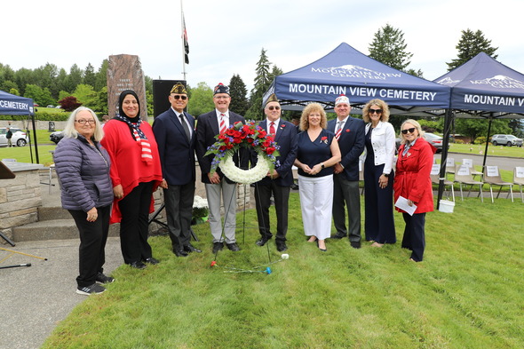 Group stands with a memorial wreath at Mountain View Cemetery during a remembrance ceremony.