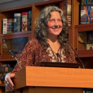 Author speaks at a podium in front of bookshelves.
