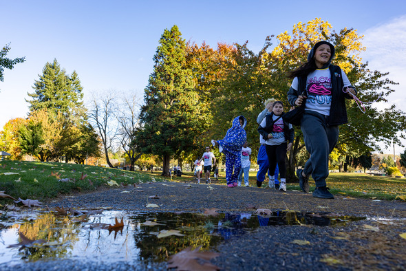 Participants in Glow Almost 5K shirts walk through an Auburn park on a sunny fall day.