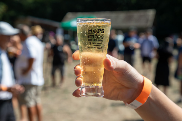 A hand holds a beer glass that says Hops and Crops 