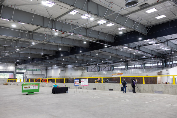 Interior of a large recycling facility with sorting bays, machinery, yellow safety railings and two people near displays.