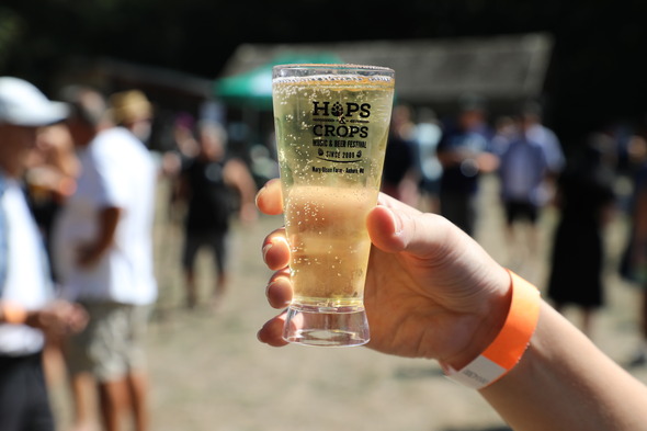 Close-up of a Hops & Crops tasting glass held up at the outdoor festival.