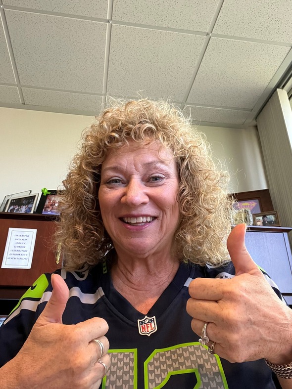 Woman wearing a Seahawks jersey smiles and gives two thumbs up.