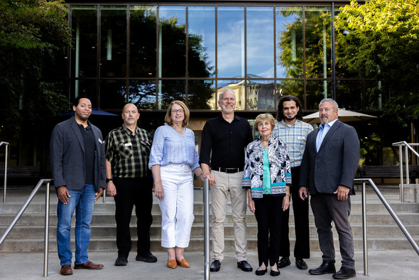 Seven people pose together on the steps outside a glass-fronted building.