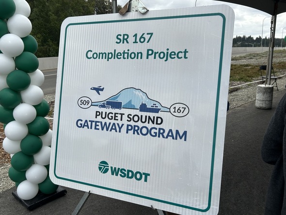 Sign for the SR 167 Completion Project and Puget Sound Gateway Program stands beside green and white balloons.