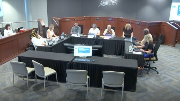 A group of people seated around a set of tables in the center of the Auburn City Hall Council Chambers 