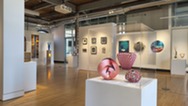 Interior of an art gallery with sculptures, paintings and mixed-media works displayed throughout the space.