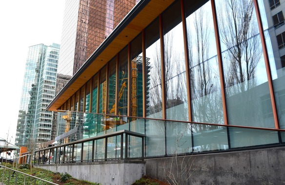 Side view of glass building with reflection of construction crane. Tall high rise buildings in the foreground.