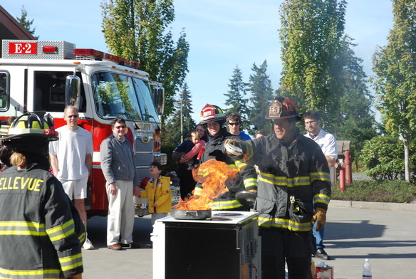 Photo shows firefighter providing a fire prevention demonstration to onlookers.