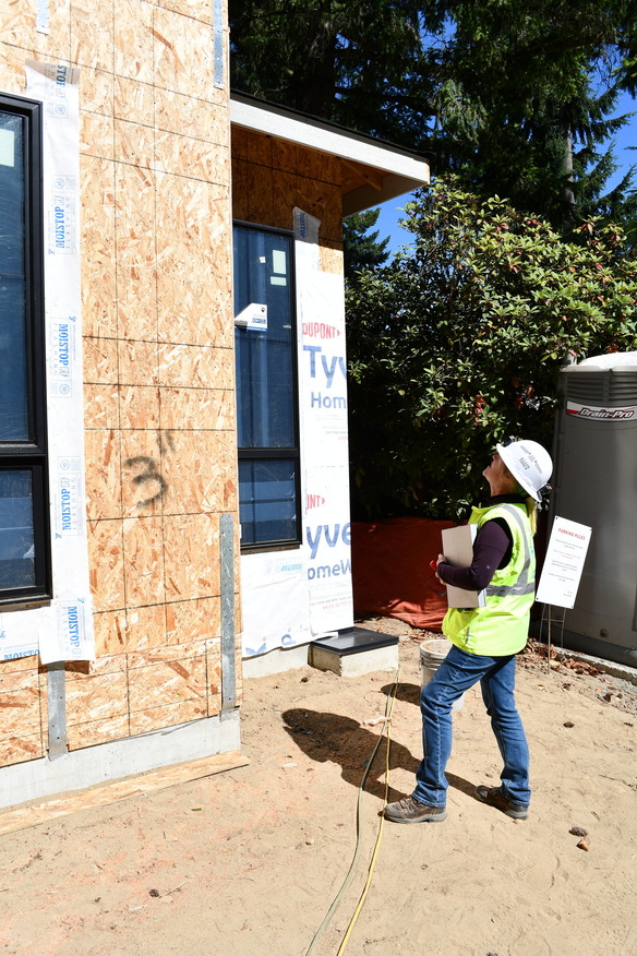 Photo shows building inspector looking at exterior of a wood framed building under construction