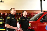 Two firefighters hold fire safety tools. 