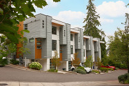 Four townhomes lined next to each other on a street, trees in foreground and background with a few cars in driveways