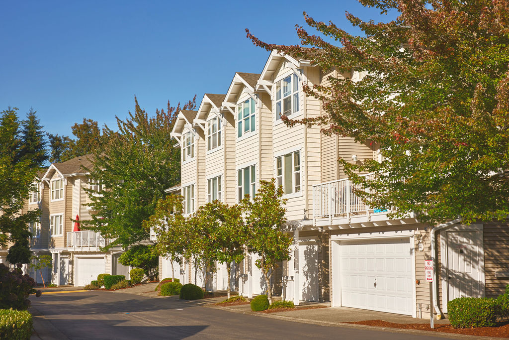 Photo shows townhomes with garages on the bottom with driveways in front. Trees and shrubs are also present. Photo by Stanton J. Stephens